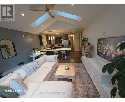 A spacious living room with a white sofa and a kitchen in the background.