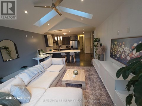 A spacious living room with a white sofa and a kitchen in the background.