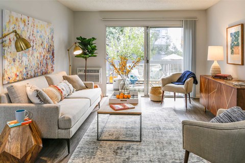 A living room with a grey sofa, a wooden side table, and a large painting on the wall.
