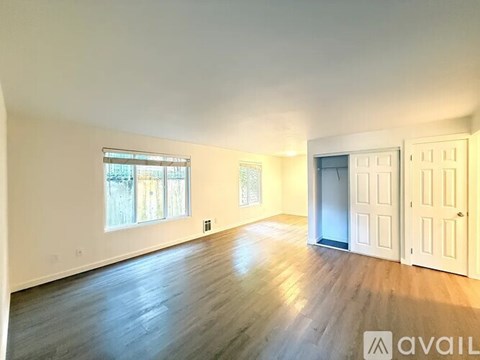 A spacious room with wooden flooring and white walls, featuring a large window and a door.
