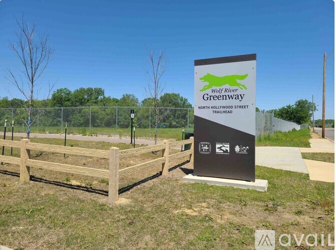 A sign for the Wolf River Greenway stands in front of a fence and a bench.