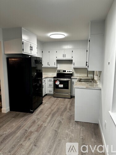 A kitchen with a black fridge, stove, and white cabinets.