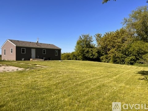 A house with a brown roof and a white door is surrounded by a grassy field.