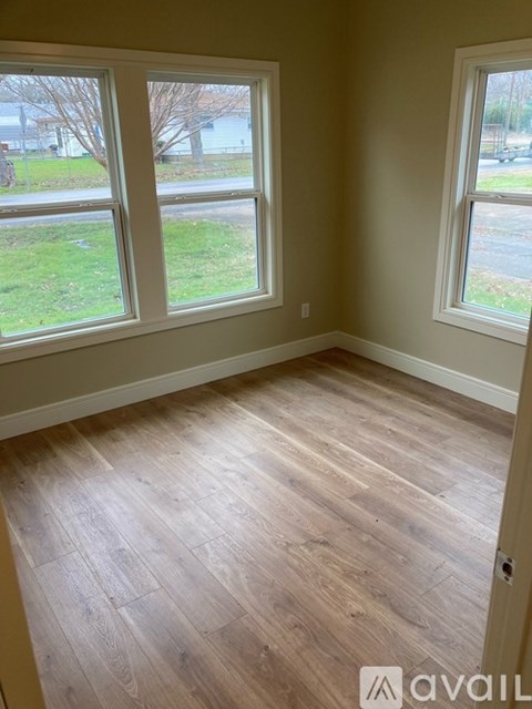 A room with wooden floors and two windows overlooking a grassy area.