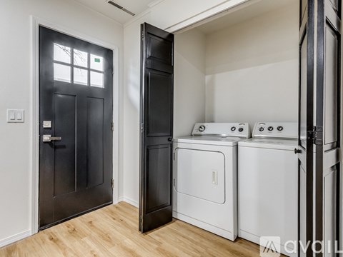 A black door is open to a room with a white wall and a wood floor.