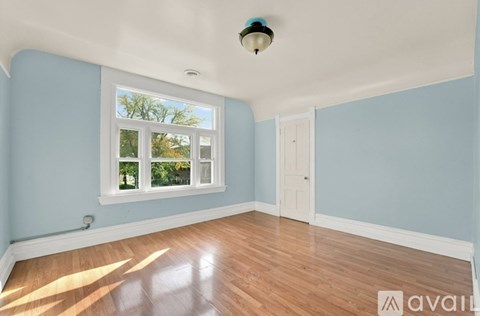 A room with light blue walls and wooden flooring, featuring a window with a view of trees and a white door.