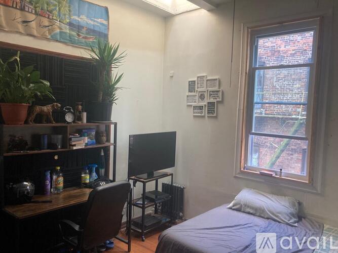 A room with a bed, desk, and a window with a view of a brick building outside.