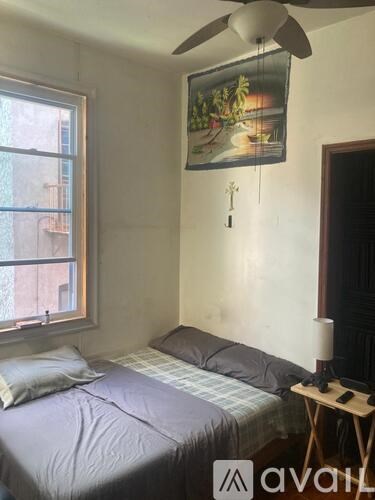 A bedroom with a bed, a ceiling fan, and a painting on the wall.