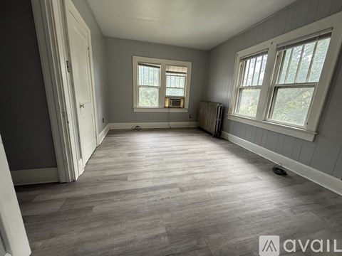 A room with grey walls and wooden flooring, featuring a window with a view of trees.