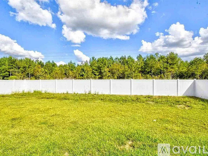 A white fence surrounds a grassy field with trees in the background.