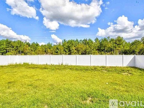 A white fence surrounds a grassy field with trees in the background.