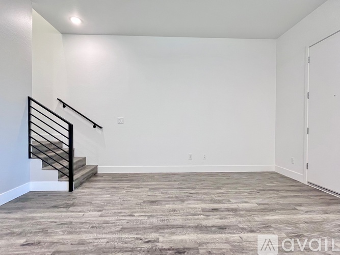 A spacious room with a wooden floor and a staircase with a metal railing.
