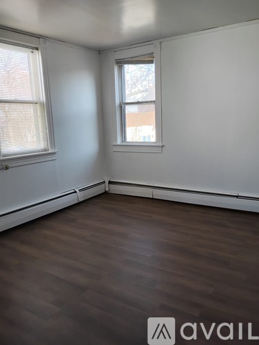 A room with wooden flooring and two windows.