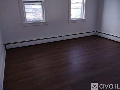 A room with dark wood flooring and two windows.