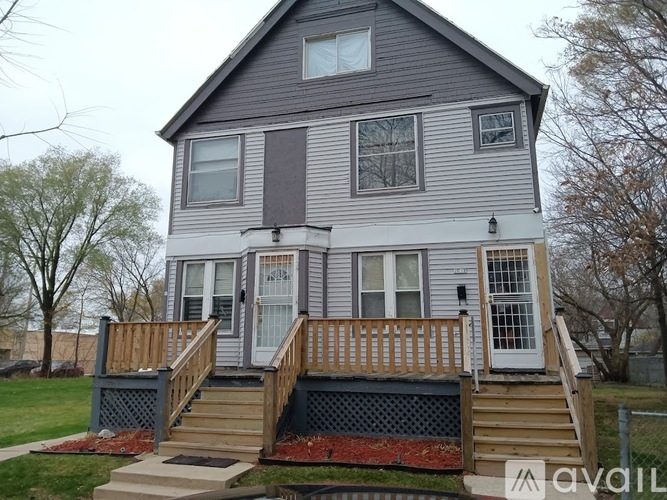 A grey house with a wooden deck and stairs leading to the front door.