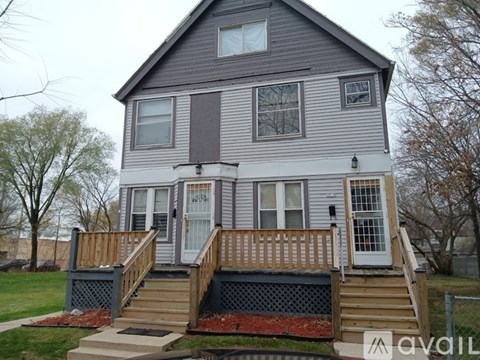 A grey house with a wooden deck and stairs leading to the front door.