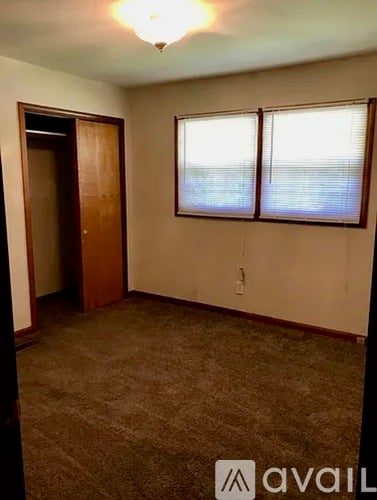A room with a carpeted floor, a door, and a window with blinds.