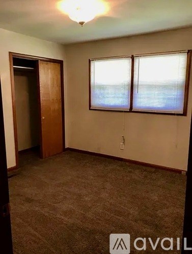 A room with a carpeted floor, a door, and a window with blinds.