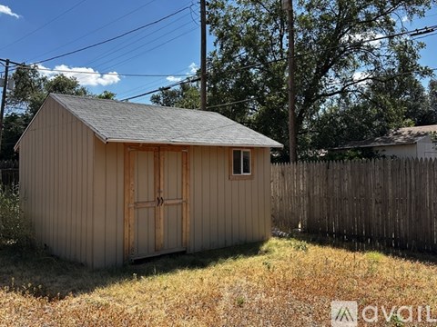 A small wooden shed with a brown door stands in a grassy field.