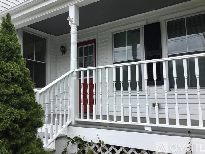 A white house with a red door and a white porch.