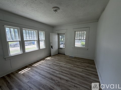 A room with wooden floors and white walls, with a door and a window.