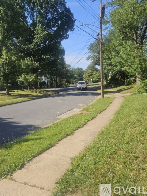 A tree-lined street with a sidewalk and a car parked on the side.