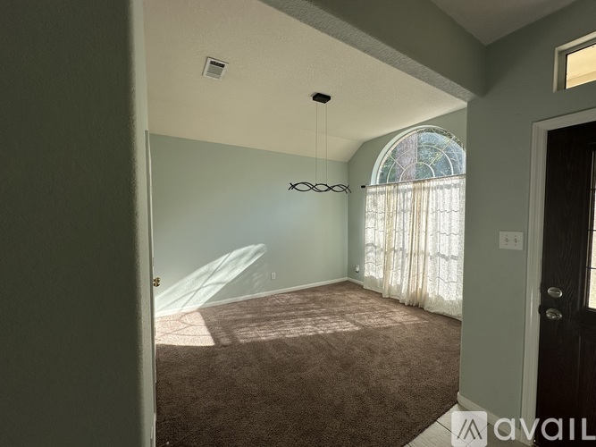 A room with a carpeted floor and a large window with white curtains.