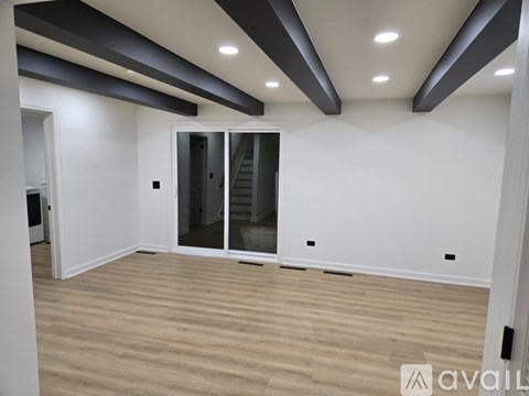 A spacious room with wooden flooring and a glass door leading to a staircase.