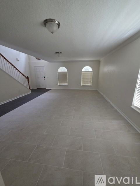 A spacious room with tiled flooring and a staircase on the left side.