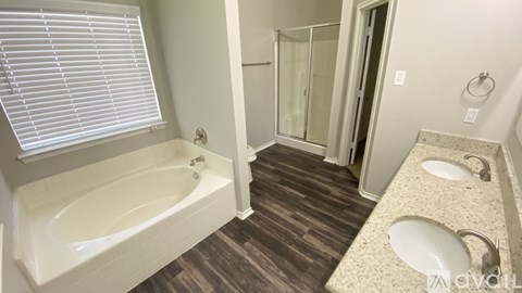 A bathroom with a white bathtub, a walk-in shower, and a double sink vanity.