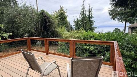 Two chairs are on a wooden deck with a railing.