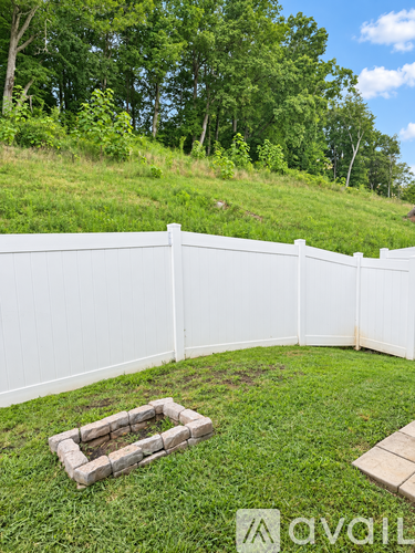 A white fence encloses a grassy area with a small fire pit.