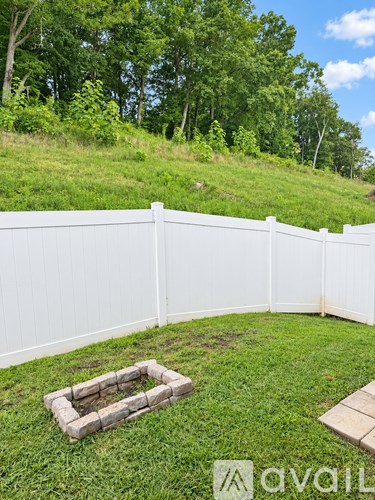 A white fence encloses a grassy area with a small fire pit.