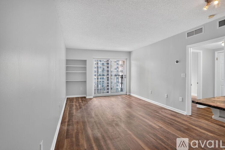 A spacious room with wooden flooring and a large window with blinds.