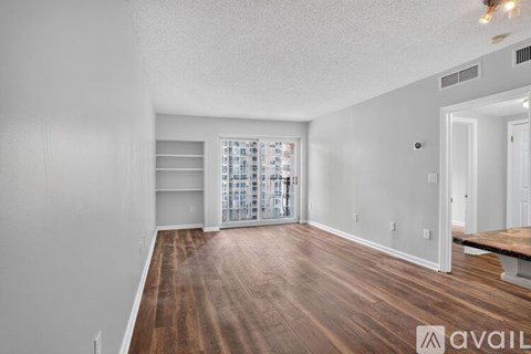 A spacious room with wooden flooring and a large window with blinds.