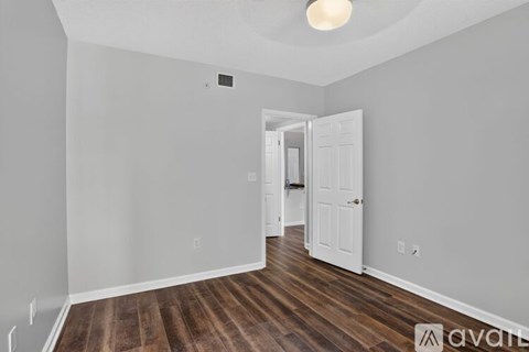 A room with wooden floors and white walls, with a doorway leading to another room.
