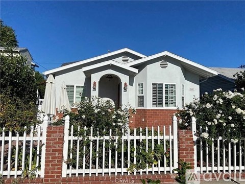 A white house with a red brick base and a white picket fence.