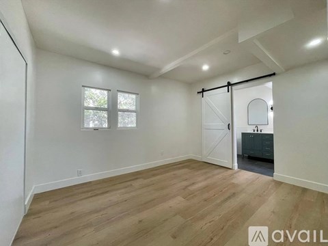 A spacious room with wooden flooring and a sliding door leading to a bathroom.