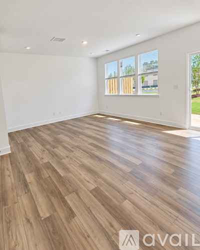 A spacious room with wooden flooring and large windows.