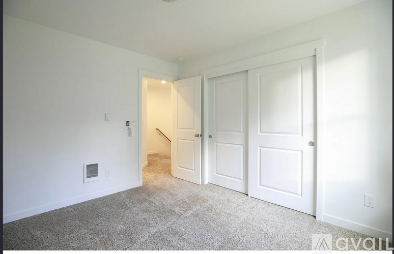 A room with white walls and a carpeted floor with a doorway leading to another room.