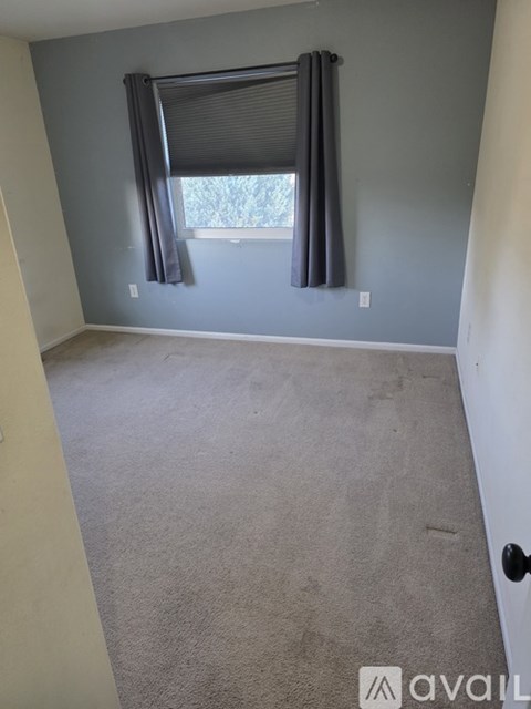 A room with a carpeted floor and a window with black curtains.
