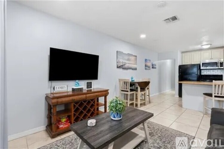 A living room with a wooden table and chairs, a flat screen TV, and a kitchen area in the background.
