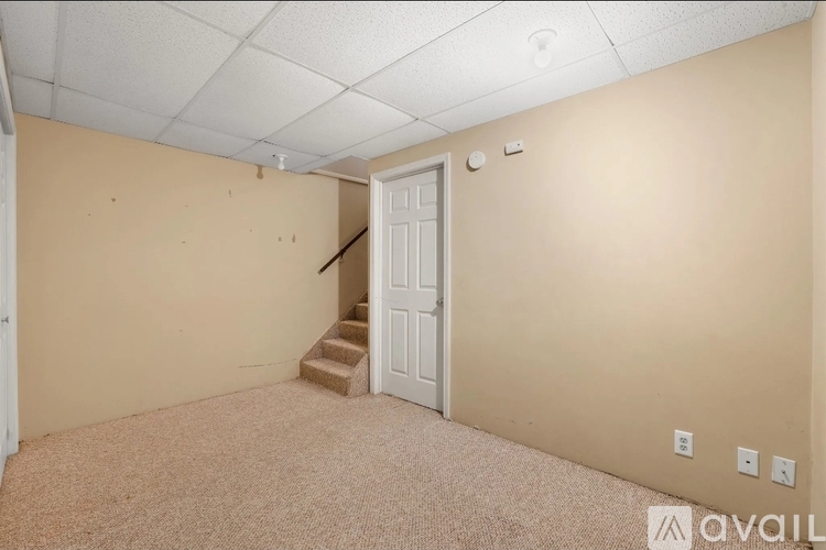 A room with a carpeted floor, a white door, and a staircase leading to another room.