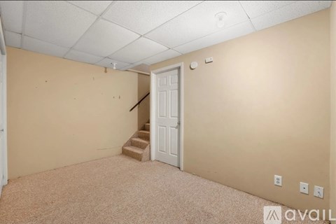 A room with a carpeted floor, a white door, and a staircase leading to another room.