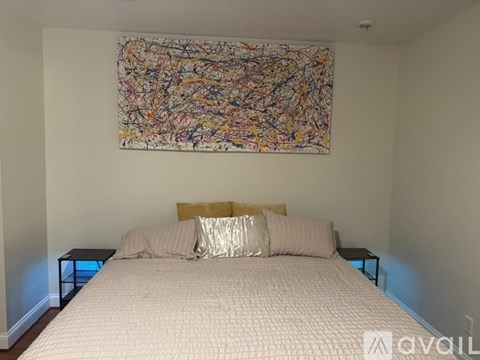 A bedroom with a large abstract painting above the bed.