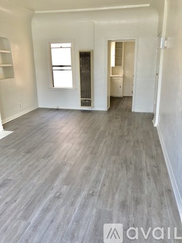 A room with wooden flooring and white walls, with a window and a door visible.