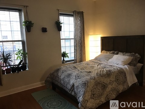 A bedroom with a bed, two hanging plants, and a window with a curtain.