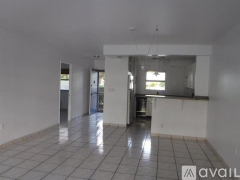 A spacious kitchen and living room with white tiled floors and white walls.