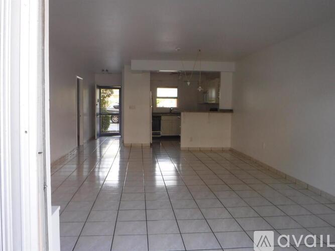 A spacious room with white tiled flooring and a kitchen area in the background.