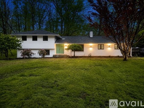 A white house with a green door and windows is surrounded by a grassy lawn and trees.